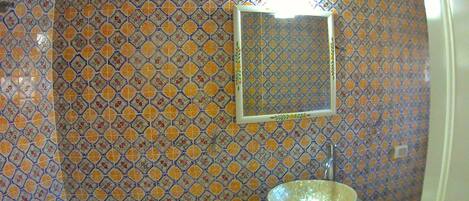 A bathroom with patterned tile walls, a sink with a bowl, and a mirror.