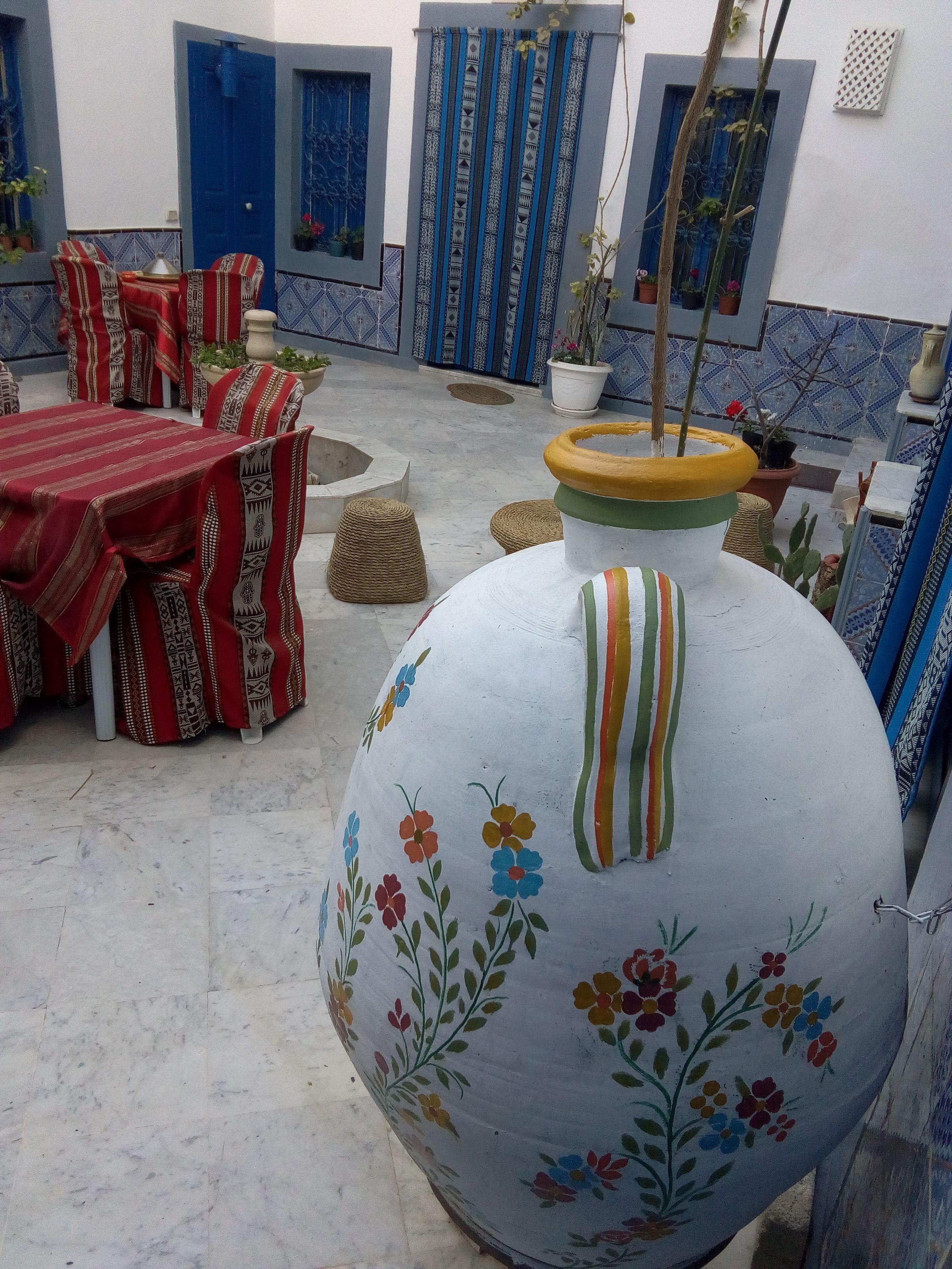 Une cour avec des sièges extérieurs, un grand vase décoratif et des murs aux motifs bleus.