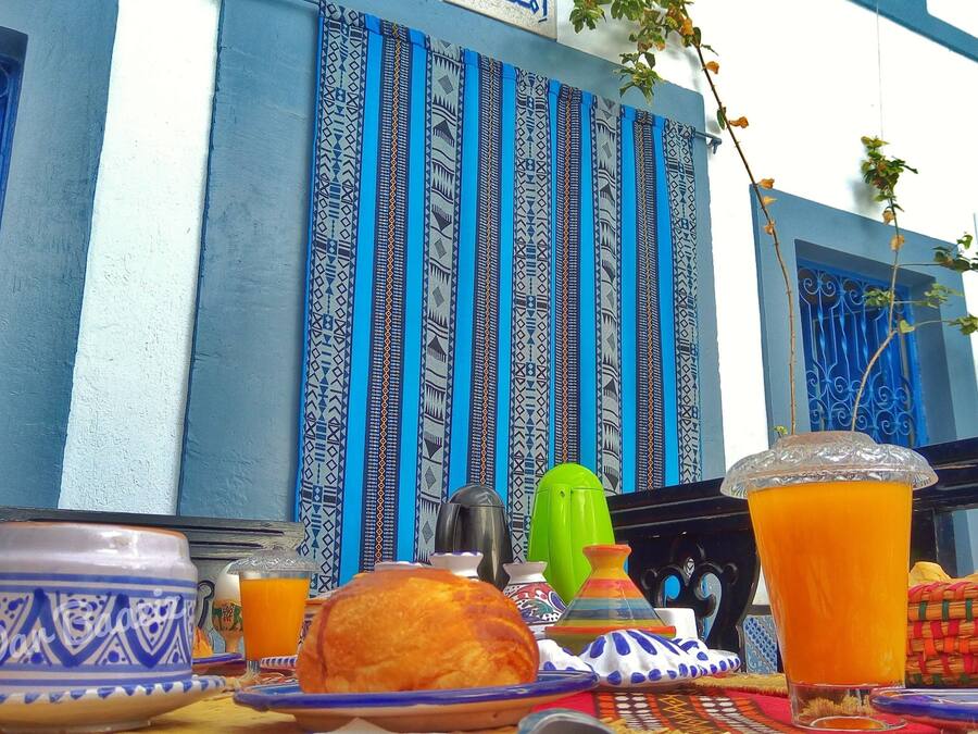 Una mesa con platos tradicionales marroquíes, un muro azul y blanco a rayas y una planta colgante.