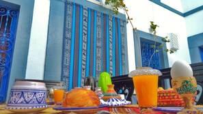 A table with traditional Moroccan dishes, a blue and white striped wall, and a hanging plant. - Dar Baaziz (Sousse)