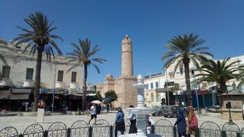 A square with a tall minaret, palm trees, and a fountain.