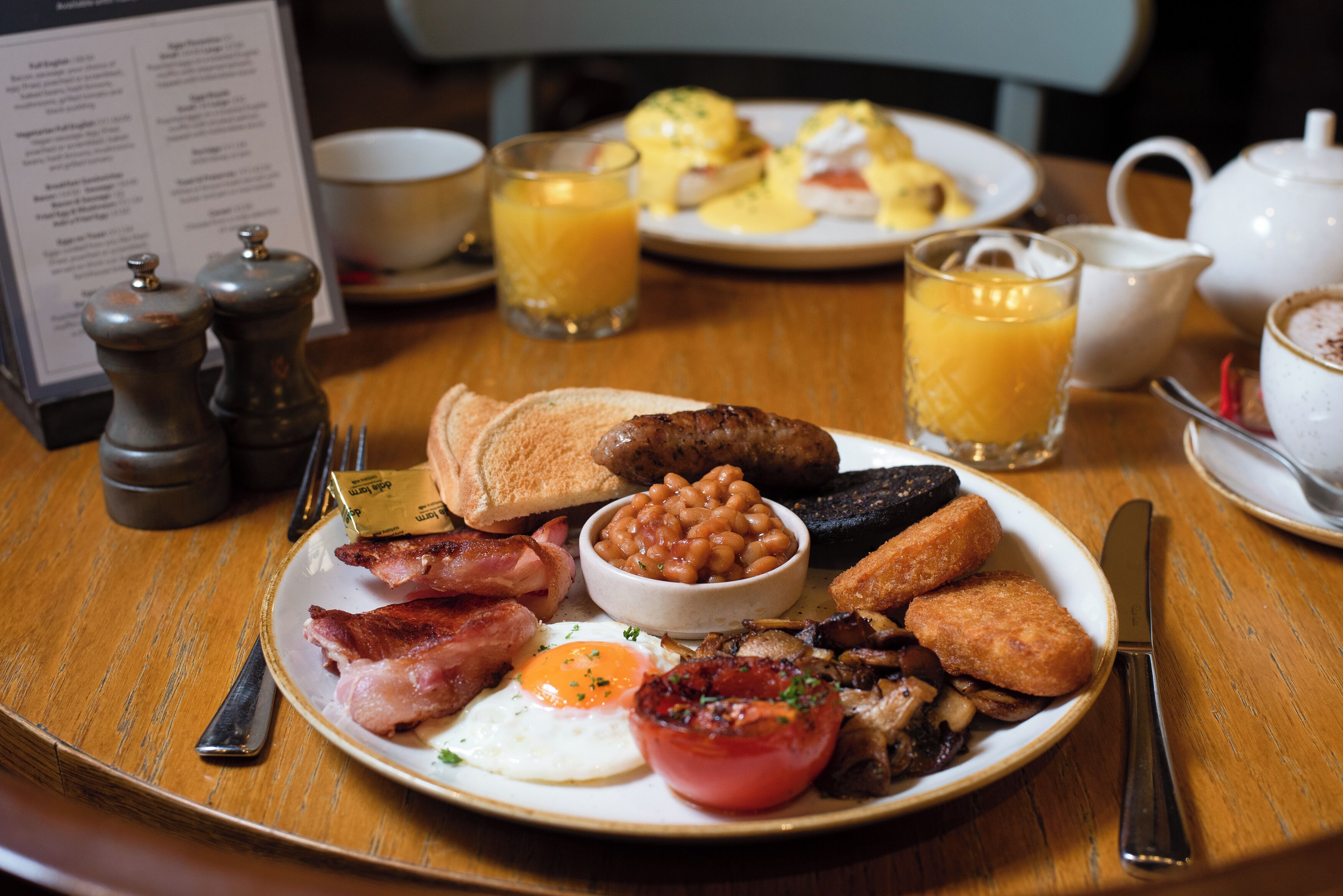 A breakfast plate with eggs, bacon, sausages, beans, mushrooms, and toast.