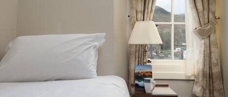Un lit bien fait, avec du linge de lit blanc, une table de chevet avec une lampe, un livre et une tasse.