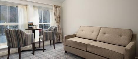 Una sala de estar con un sofá color beige, sillones a rayas, alfombra escocesa y vistas amplias a través de grandes ventanales.