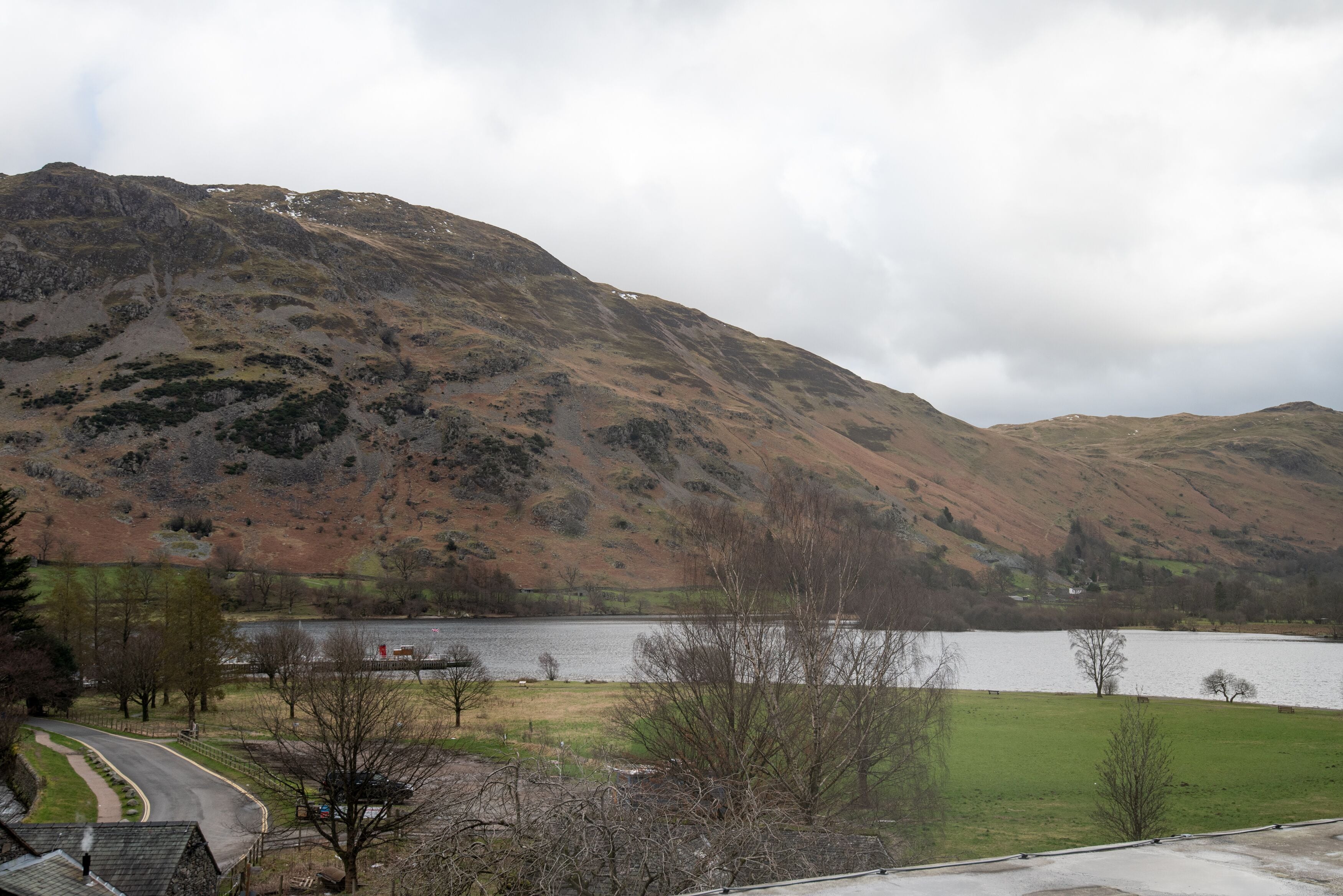 A mountainous landscape with a lake, a road, and a building in the foreground.