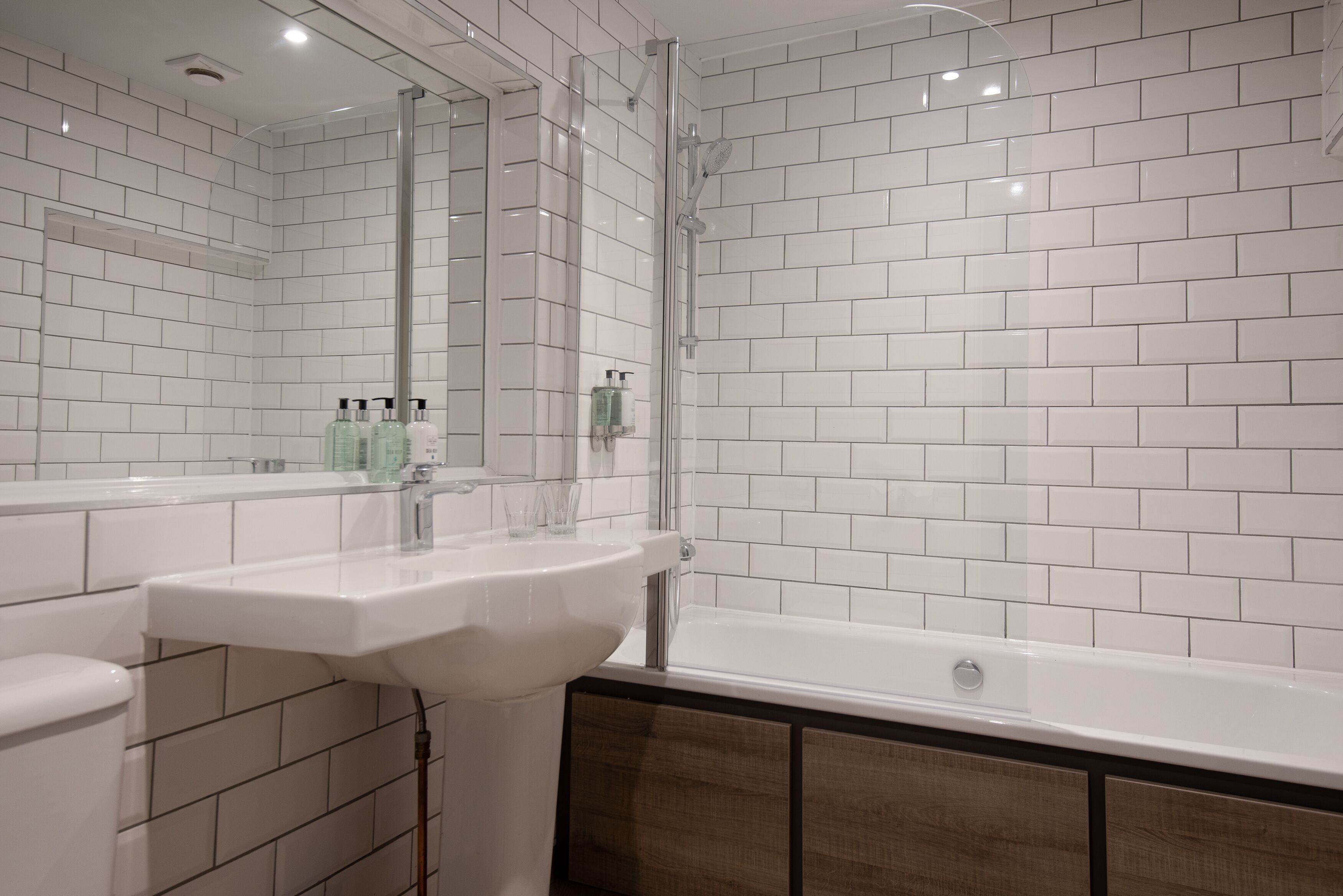A modern bathroom with white tiled walls, a white sink, and a bathtub.