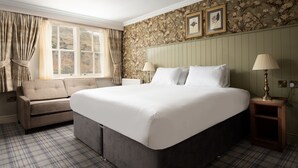 A bedroom with a large bed, a sofa, a window with curtains, and a floral wallpaper. - The Ullswater Inn- The Inn Collection Group (Penrith)