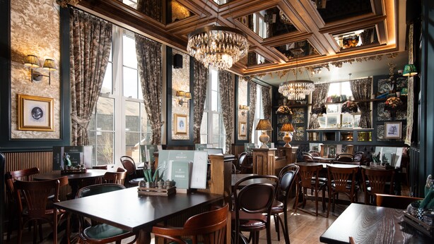 A dining area with wooden tables and chairs, chandeliers, and framed pictures on the walls. - The Ullswater Inn- The Inn Collection Group (Penrith)