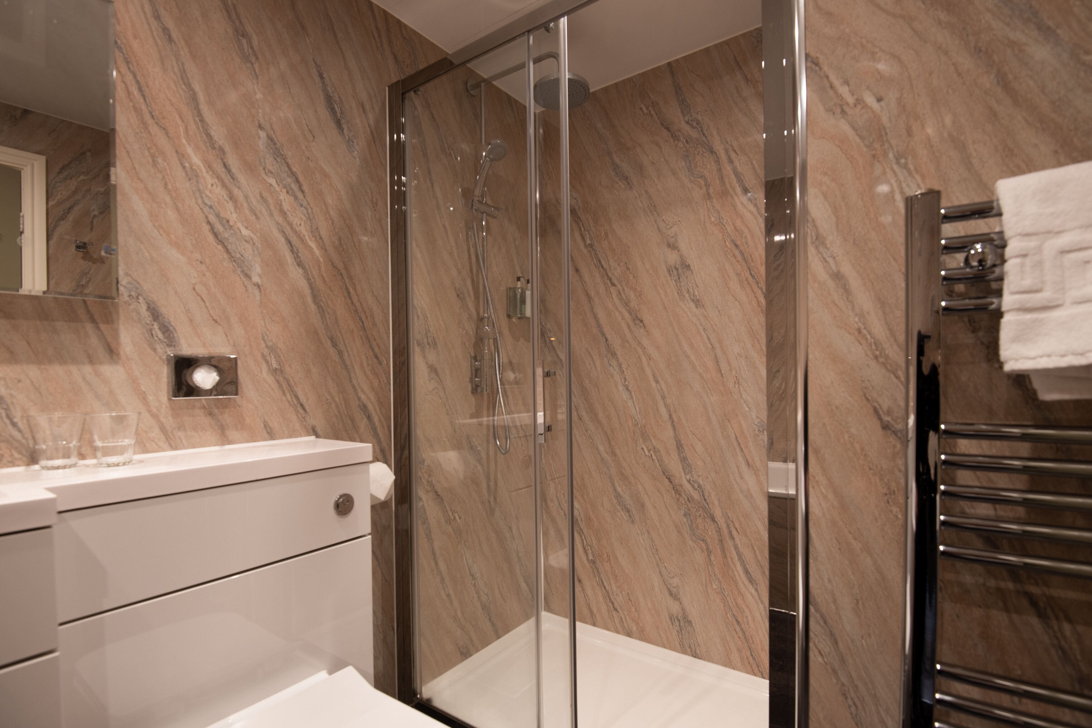 A modern bathroom with a glass-enclosed shower, marble walls, and a white vanity with drawers.