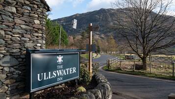 Señal de 'The Ullswater Inn', con un edificio de piedra y una vista de una montaña al fondo.