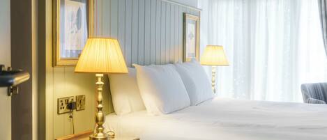 Una habitación de hotel con una cama grande, dos lámparas de noche, una mesita de noche y una ventana con cortinas.