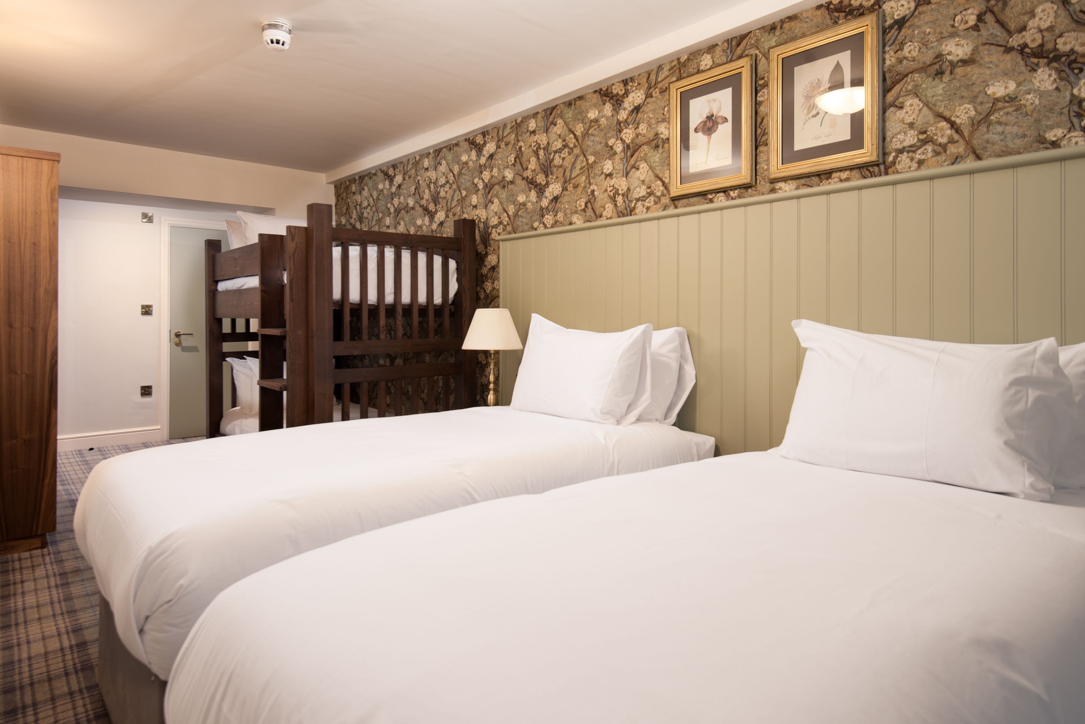 A hotel room with two beds, a wooden bunk bed, a stone-patterned wall, and framed pictures.