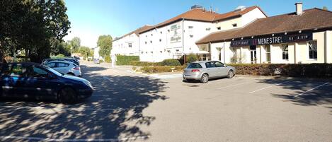 A hotel with a parking lot, a restaurant named "LE MENESTREL," and a building with a sign that reads "HOTEL de la Chandeleur."