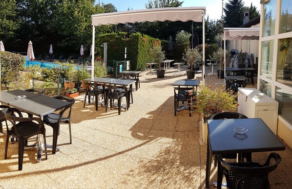 Eine Außenpatio-Terrasse mit Tischen und Stühlen, ein überdachter Sitzbereich und ein Pool im Hintergrund.