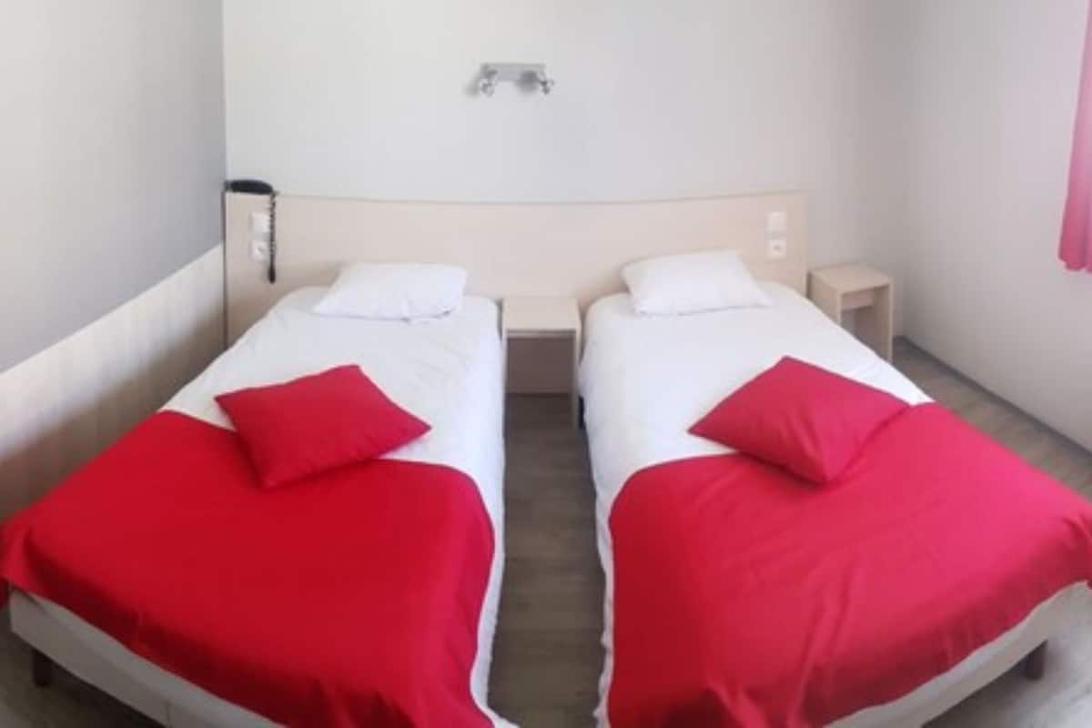 Une chambre d’hôtel avec deux lits simples, chacun étant équipé d’une couverture et d’un oreiller rouges.