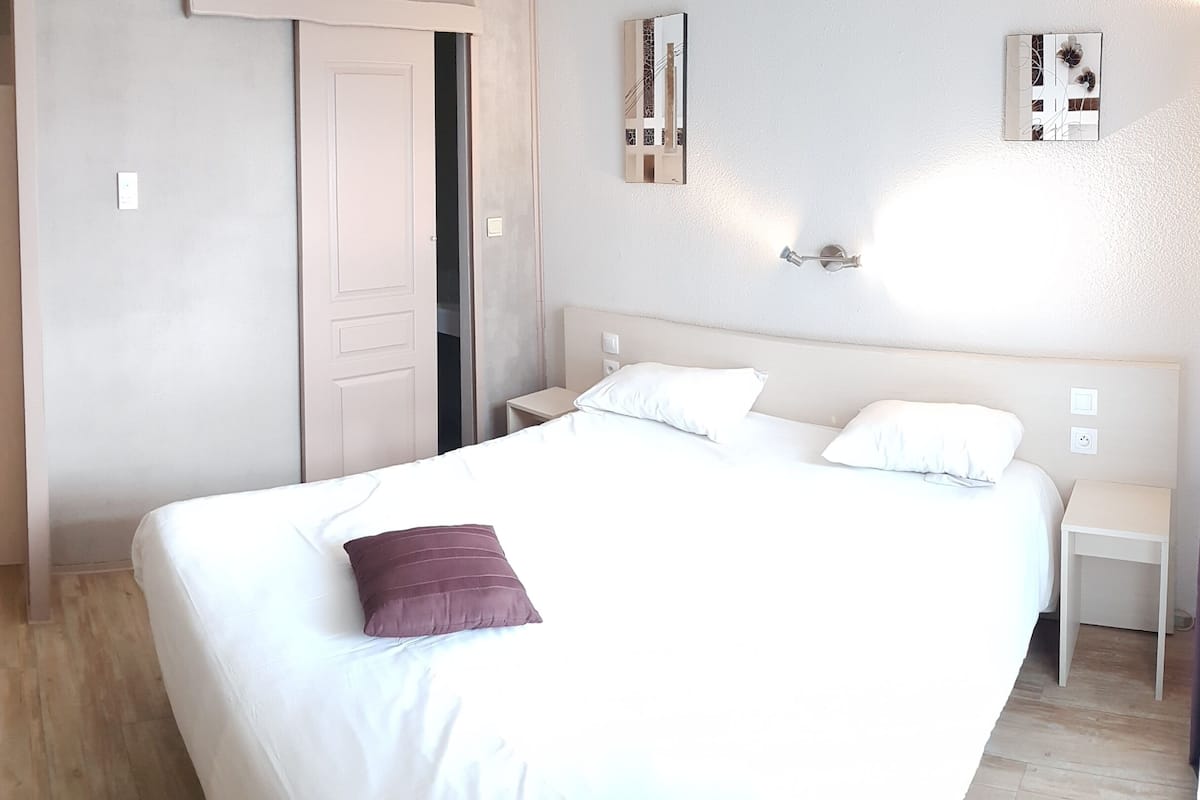 Une chambre d’hôtel avec deux lits simples, un grand lit, une table de chevet et une commode, ainsi qu’une porte donnant sur une autre pièce.