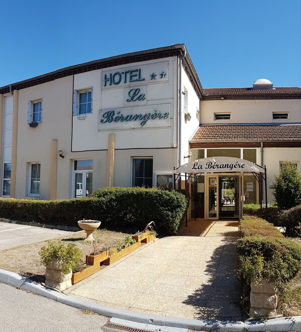 A hotel named "La Bérangère" with a sign above the entrance, a small garden area with plants, and a clear blue sky. - Hôtel la Bérangère (Perouges)