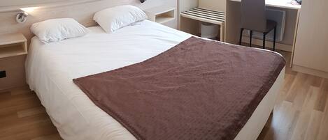 A neatly made bed with a brown blanket, a bedside table, a chair, and a desk with a chair.