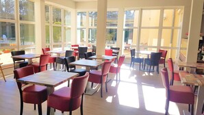 A spacious indoor area with multiple tables and chairs arranged for dining. Large windows allow natural light to fill the space. - Hôtel la Bérangère (Perouges)