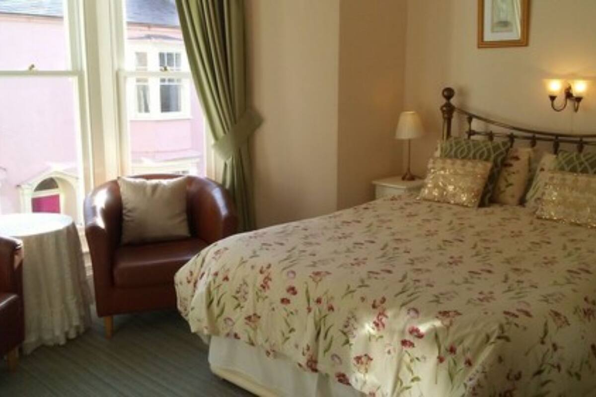Une chambre à coucher comprenant un lit, une chaise, une table de chevet et une fenêtre avec des rideaux.