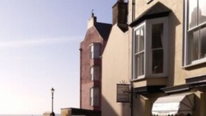 A coastal street with buildings, including a pub with outdoor seating and a lamp post. - Myrtle House Hotel (Tenby)