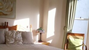 A bedroom with a bed, a nightstand, a lamp, a chair, and a window with curtains. - Myrtle House Hotel (Tenby)