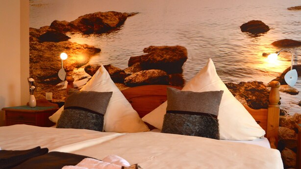 Een bed met kussens, een nachtkastje met een lamp, en een muur met een mural van rotsen en water.
