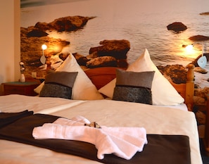 A bed with pillows, a bedside table with a lamp, and a wall with a rock and water mural.