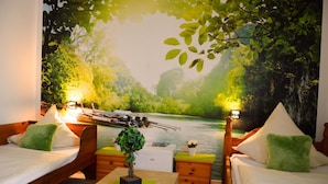Een kamer met twee houten bedden, een kleine tafel en een muurschildering van een rivier en bos.