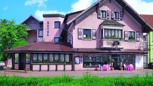 Een roze gebouw met een balkon, een bordje met daarop 'Hotel' en een aangrenzend groen gebouw.