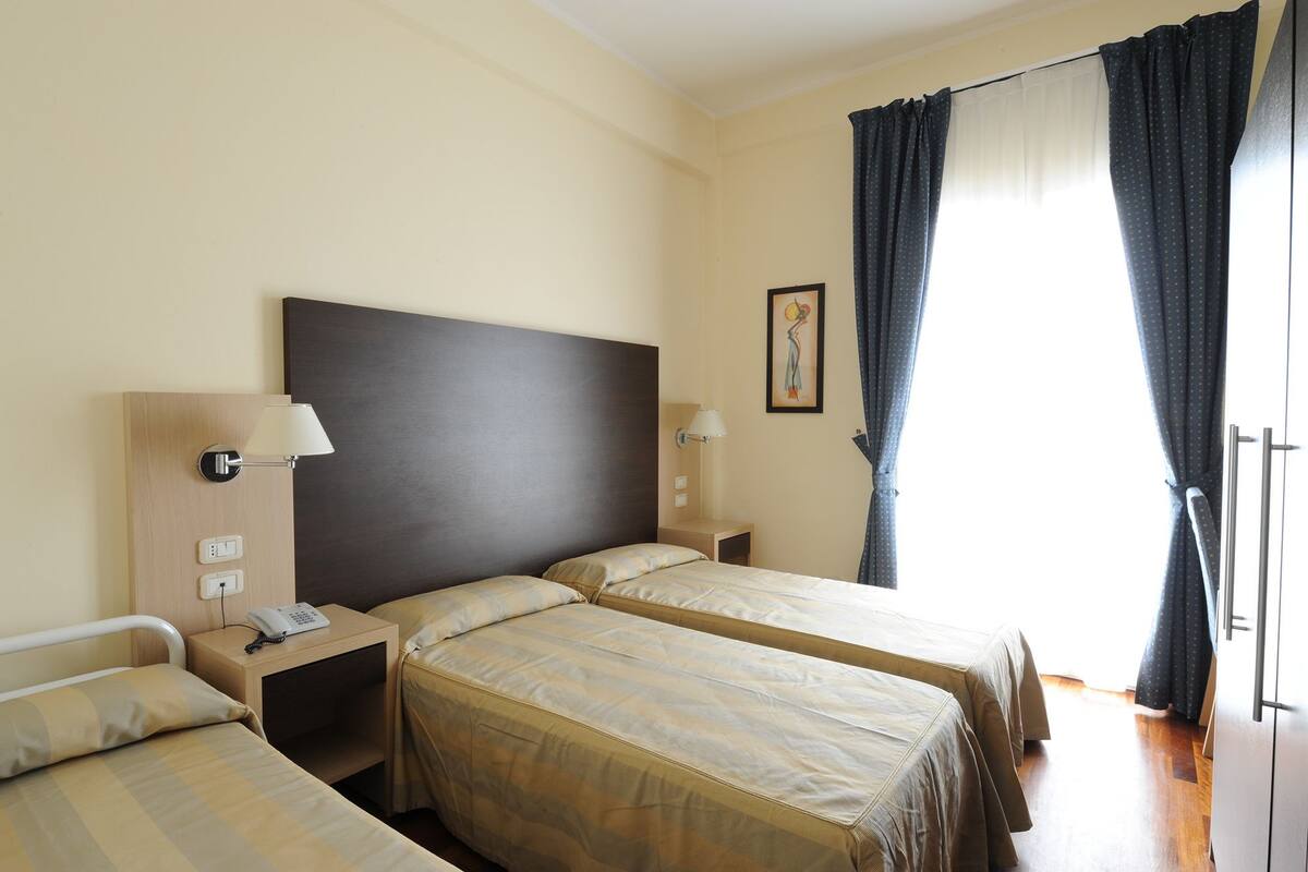 A hotel room with two beds, a dark headboard, bedside lamps, a telephone, and a window with curtains.