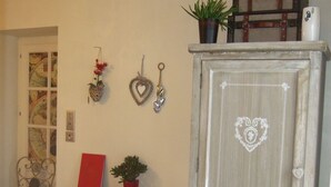 Una habitación con un armario de madera con un diseño de corazón en la puerta, un tocador con cajones, una silla, un mapa en la pared y objetos decorativos que incluyen una planta y adornos con forma de corazón.
