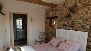 Un dormitorio con pared de piedra, una cama con ropa de cama floral, una silla y una mesita de noche con una lámpara roja.