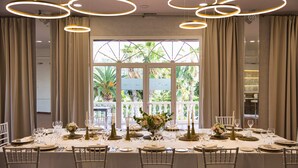 Un comedor formal con una mesa dispuesta para una comida, rodeada de sillas y un amplio ventanal con cortinas.