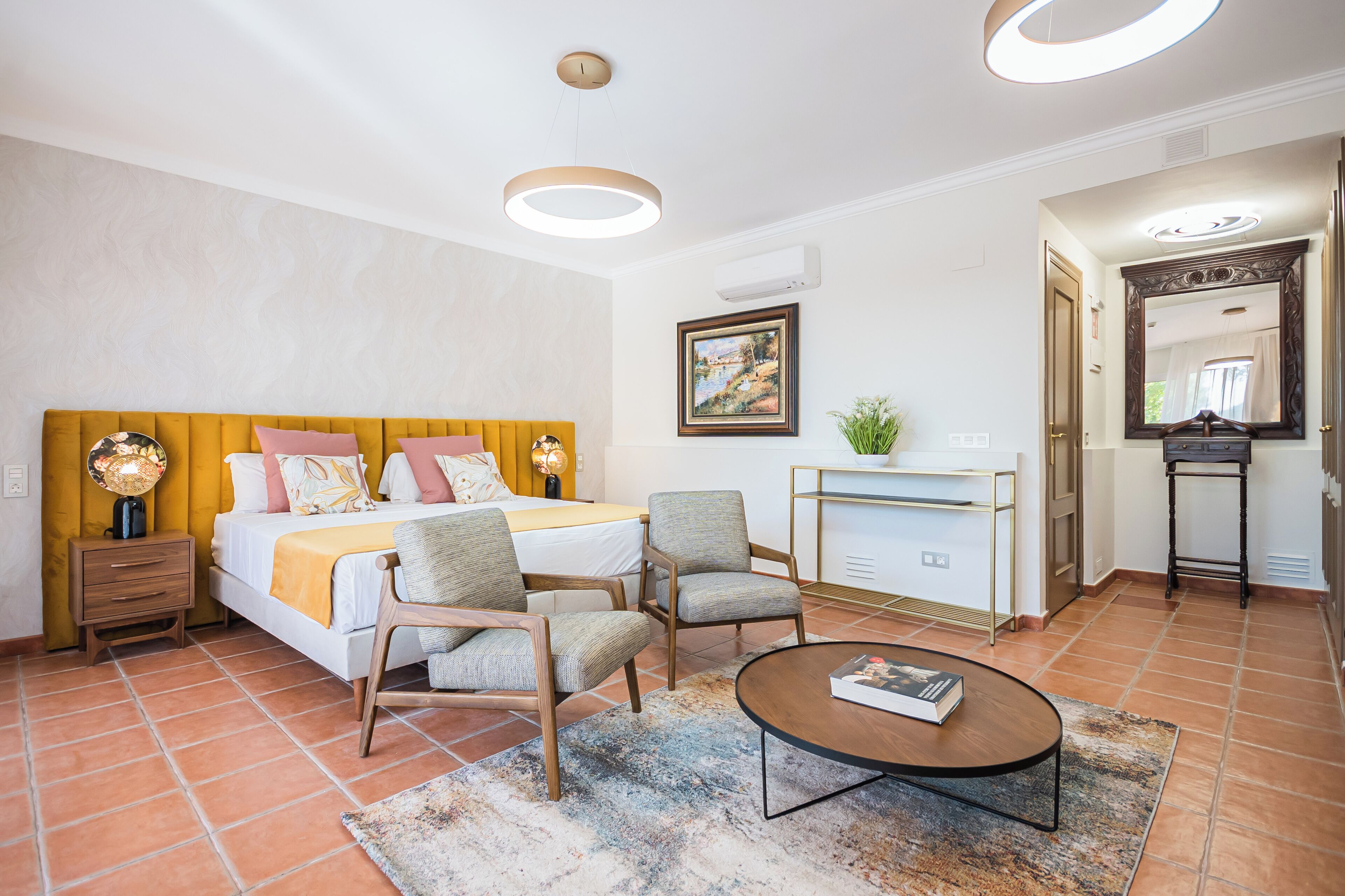A hotel room with a bed, two armchairs, a coffee table, a desk, and a mirror.
