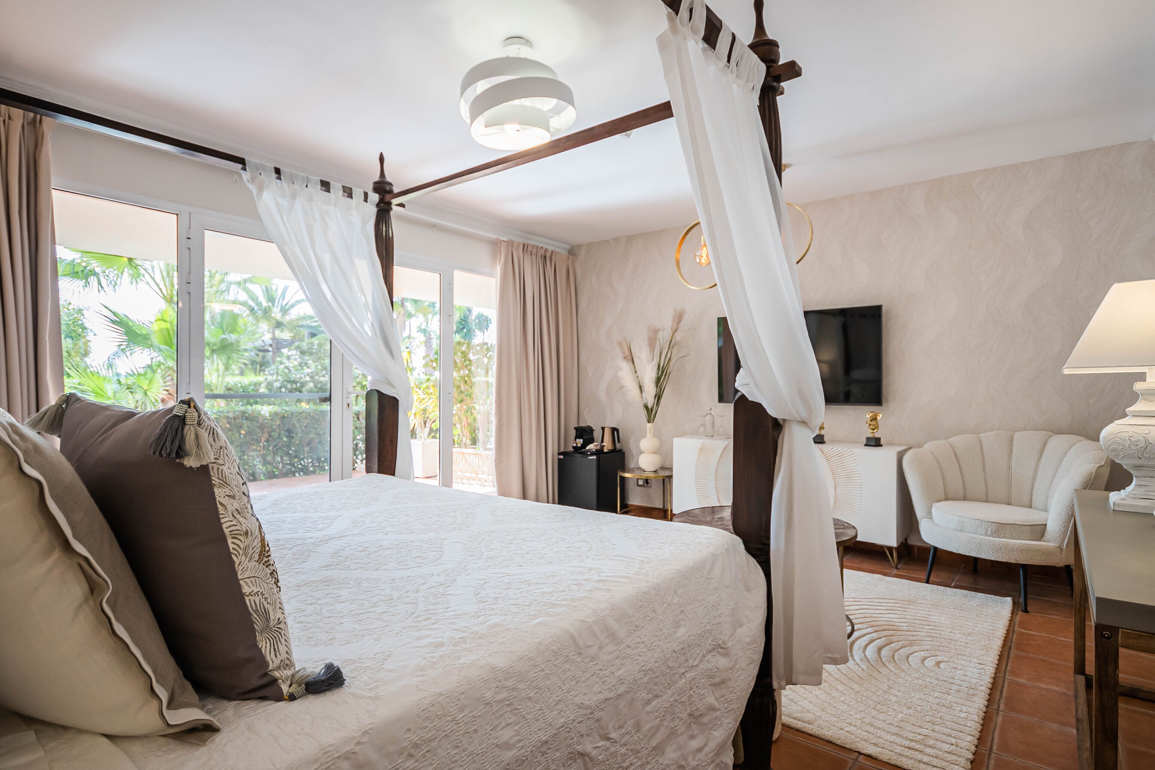 Un dormitorio con una cama grande, dosel, televisor, sillón y escritorio.