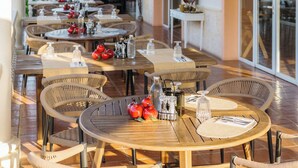 Un espacio de comedor al aire libre con mesas y sillas de mimbre, arreglos florales colgantes y vistas al jardín.