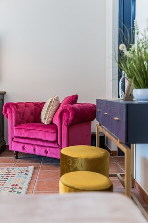 A pink tufted sofa with a decorative pillow, a small yellow ottoman, and a dark blue dresser with a plant on top. - Boutique Hotel La Plantación  (Finestrat)