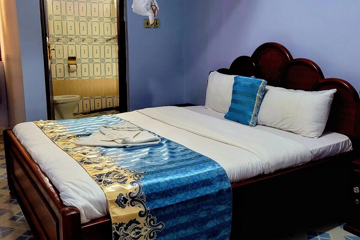A neatly made bed with a blue and white bedspread, a wooden headboard, and a white canopy.