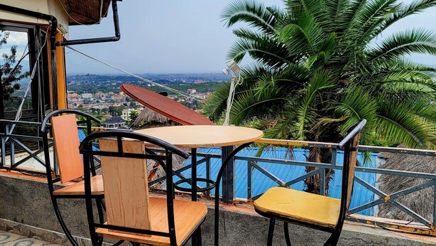 Una terraza con dos sillas de madera y una mesa, con vistas a un paisaje urbano y palmeras.