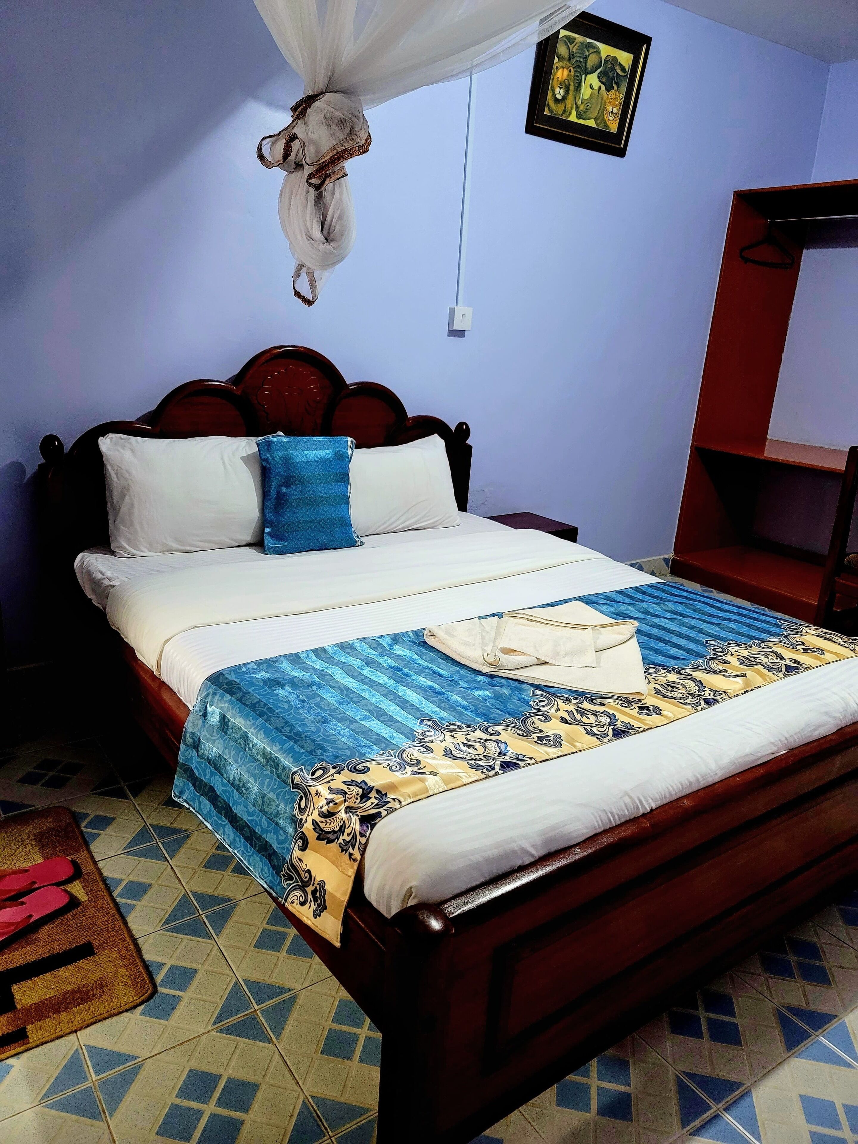 Een netjes opgemaakt bed met een deken met blauw en gele patronen, witte kussens en een witte hemel.