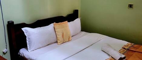 A neatly made bed with white linens and a patterned blanket, a bedside table with a lamp, and a wall-mounted light fixture.