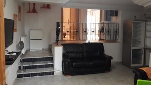 Ein Wohnzimmer mit einem schwarzen Ledersofa, einem weißen Kühlschrank, einem schwarzen Fernseher und einer Glasvitrine.