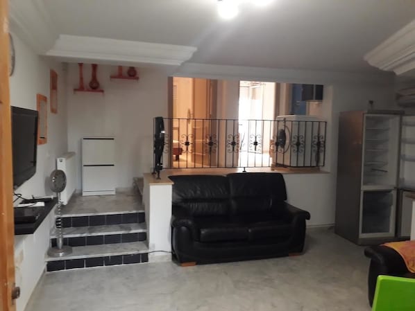 A living room with a black leather sofa, a white refrigerator, a black TV, and a glass cabinet.