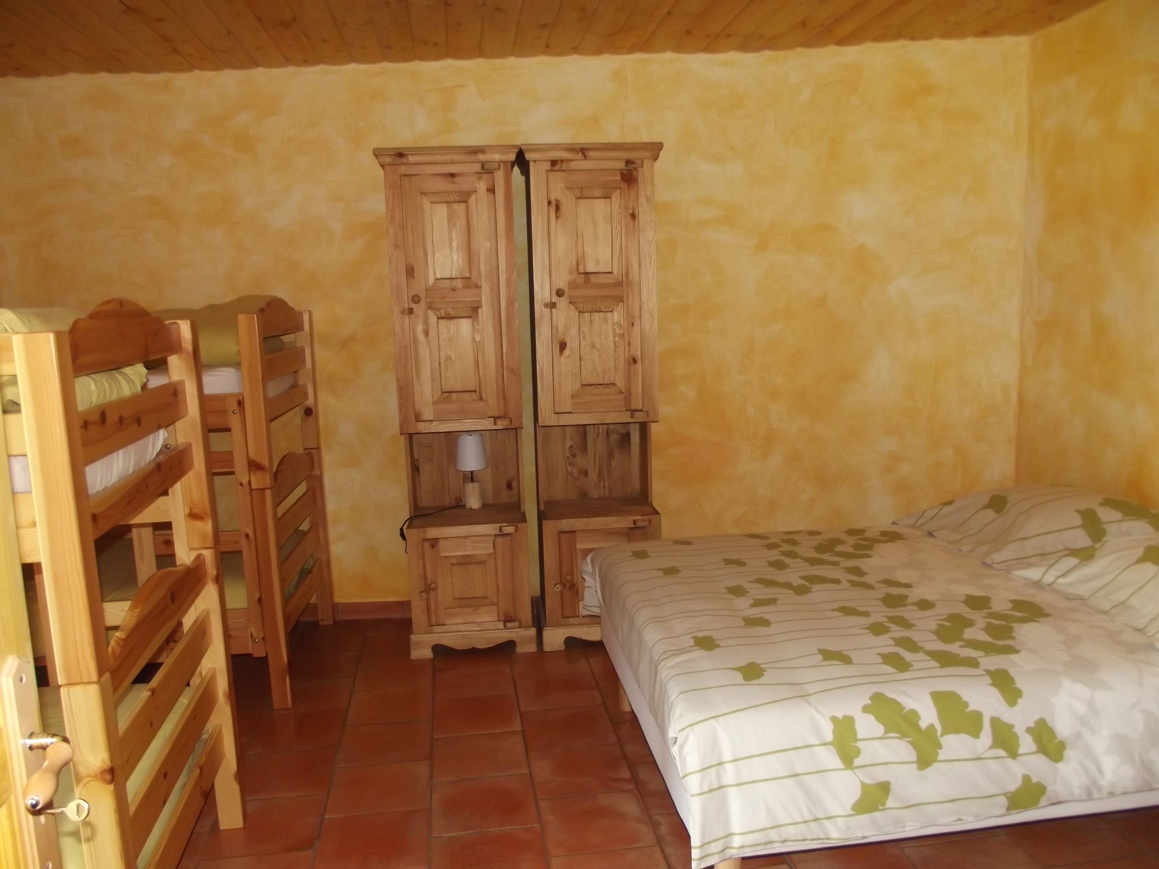 A bedroom with a bed, wooden wardrobe, and a built-in shelf unit.