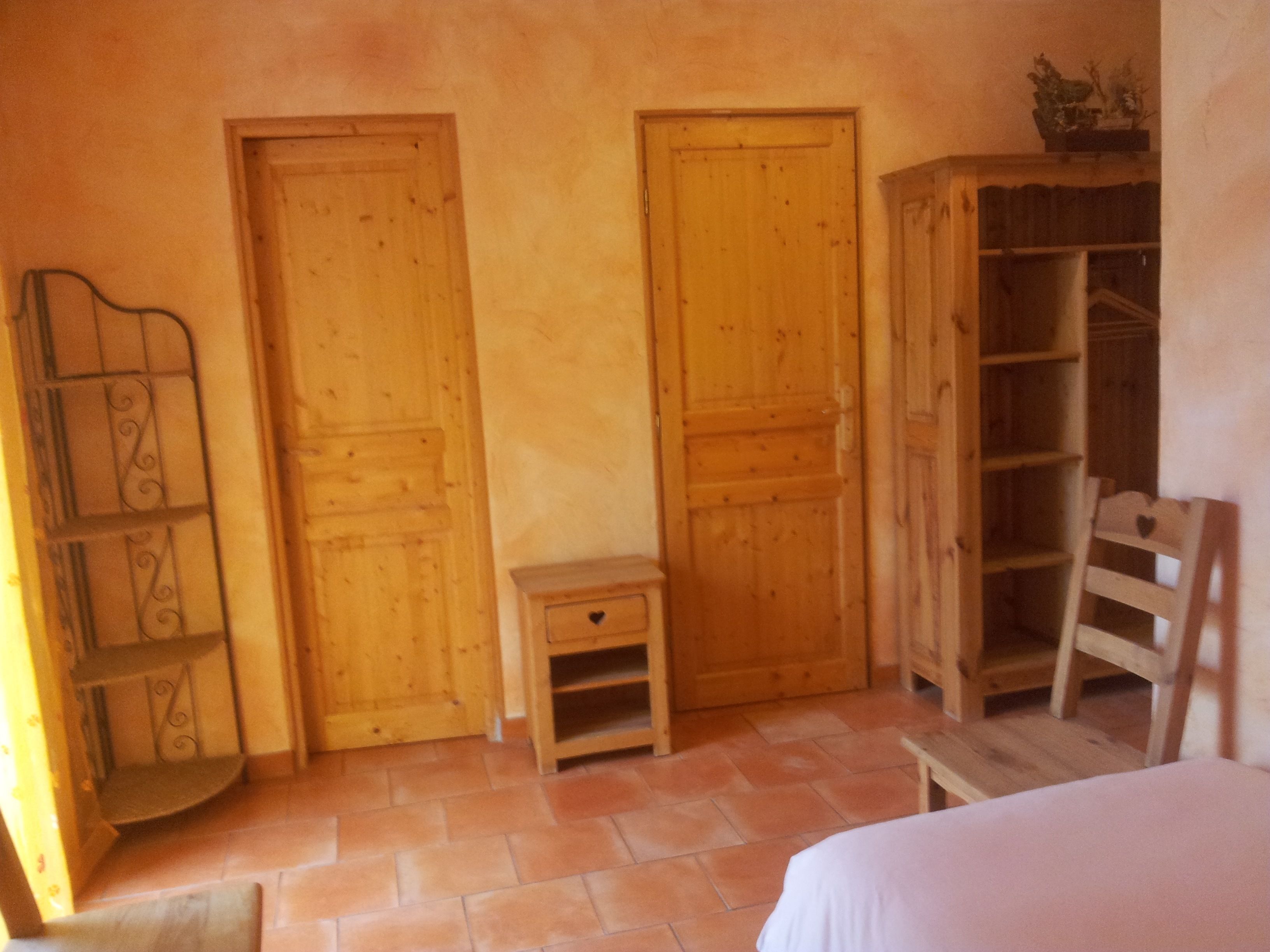 A room with wooden doors, a small wooden cabinet, a chair, and a bed.
