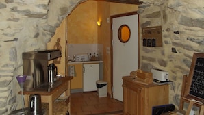 Una cucina rustica con pareti in pietra, un bancone in legno, una macchina da caffè, un tostapane e una lavagna con scritte.