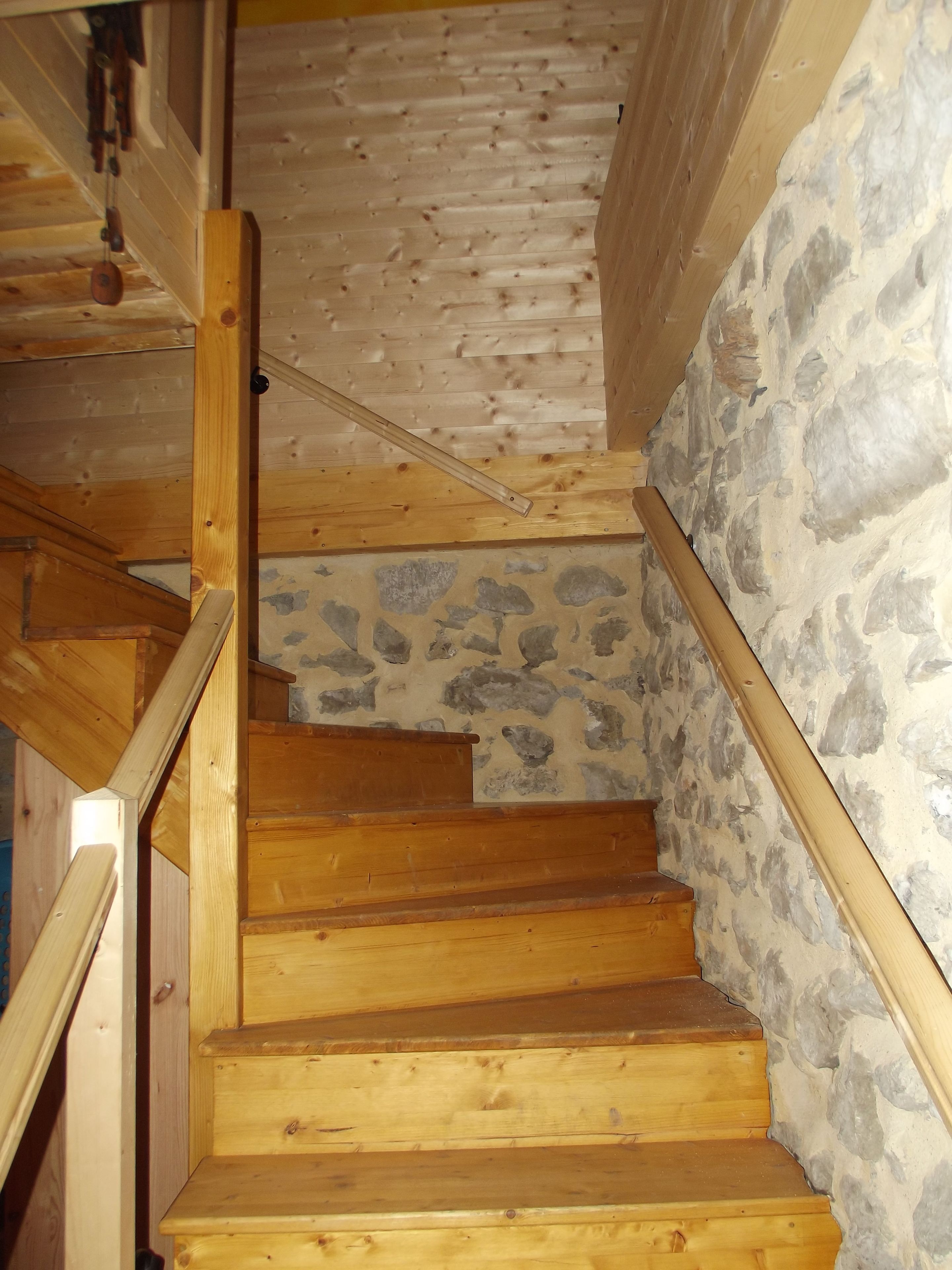 A wooden staircase with stone walls and a wooden handrail.