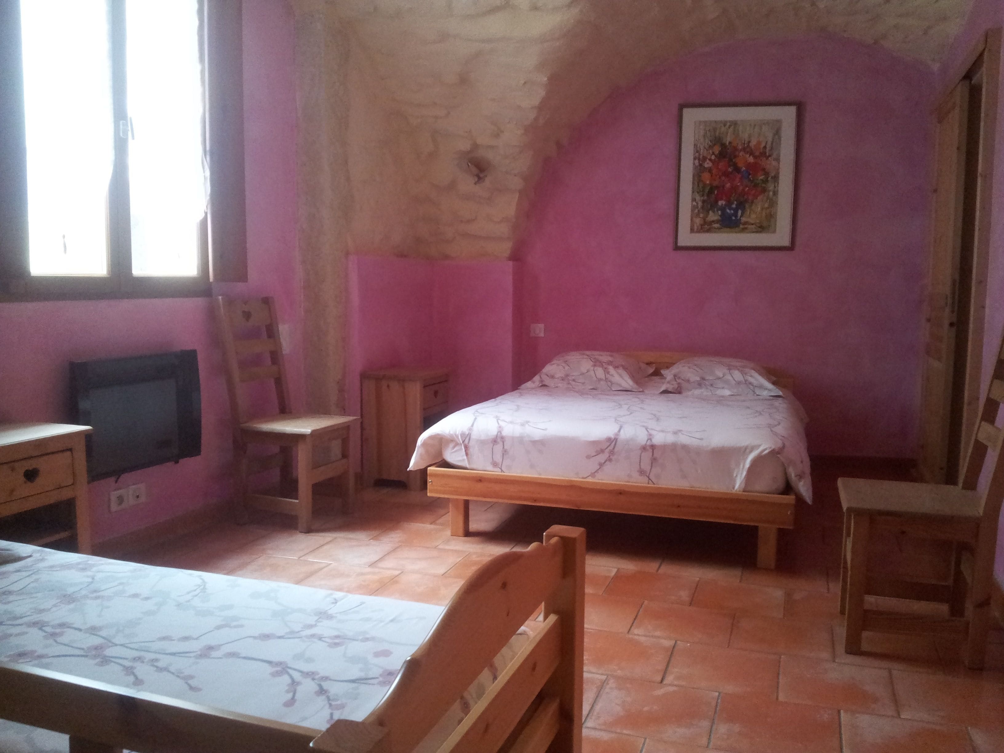 Una camera da letto con un letto, una scrivania, una sedia, una televisione e un quadro appeso al muro.