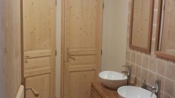 Un baño con dos puertas de madera, un tocador de madera con lavamanos y una pared con azulejos.